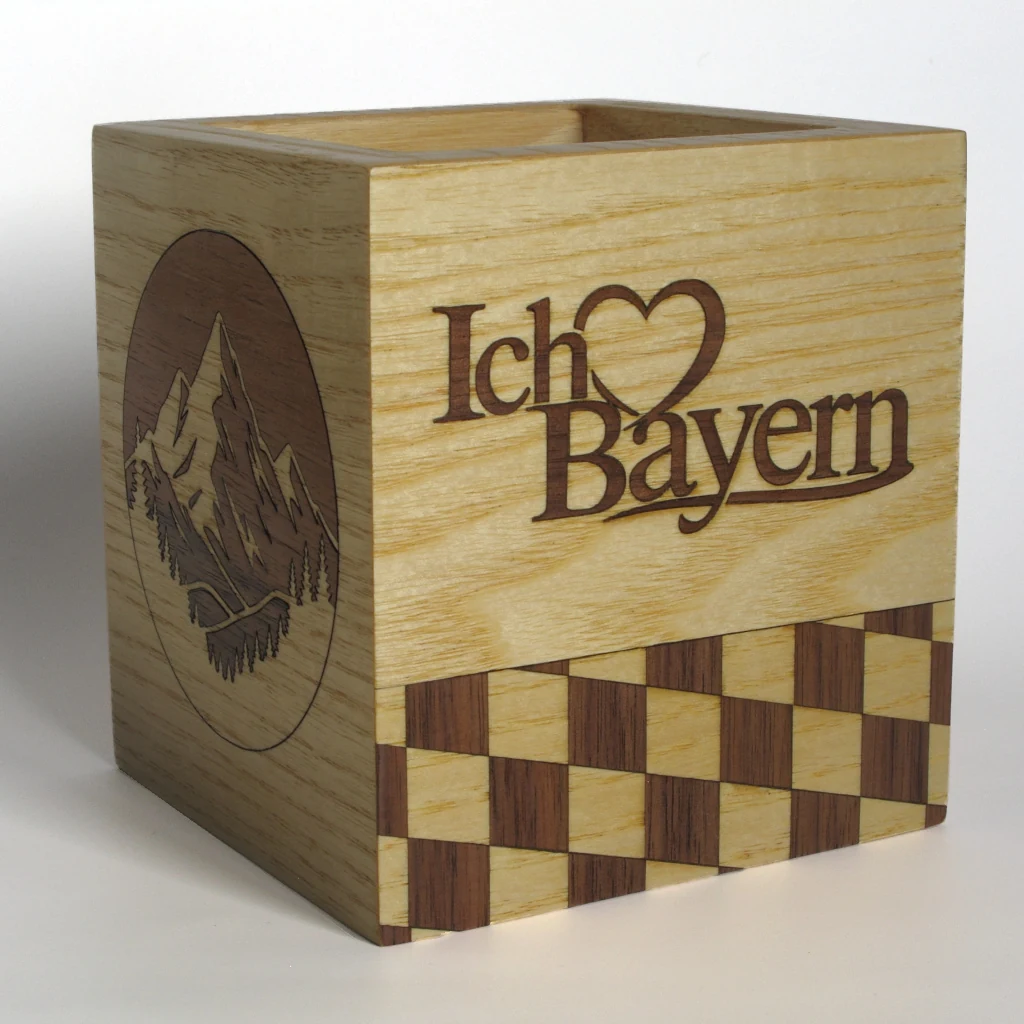 Der Stiftehalter Ich ♥ Bayern in der hellen Ausfuehrung von schraeg vorn: Schriftzug mit Herz, darunter Rautenmuster, links das Bergpanorama